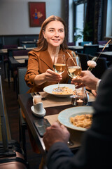 Smiling woman and cropped man toasting wine from glasses in hotel restaurant