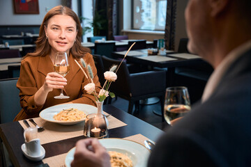 Adult happy woman and cropped man toasting wine from glasses in hotel restaurant