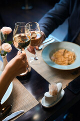 Cropped image of couple toasting wine from glasses at table in hotel restaurant