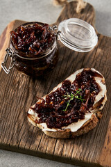 Delicious French Appetizer Freshly Cooked Onion Confit on toast with cream cheese and thyme. Wood board and jar with onion marmalade. Concrete loft background. 