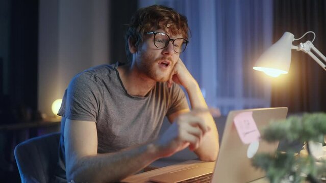 Handsome red haired man student or freelancer thinks questioningly and finding solution and typing on laptop computer at home at late night Idea pointing forward index finger concept