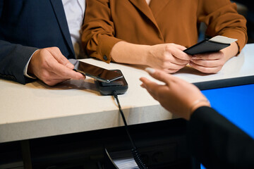 Cropped of man paying on terminal with smartphone near woman at desk in hotel