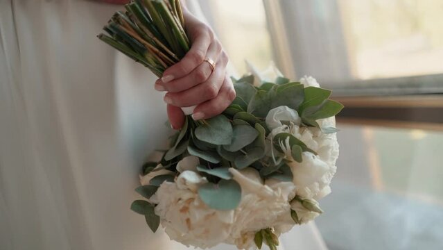 A bride with a wedding ring on her hand strokes and admires her wedding bouquet of flowers, close-up