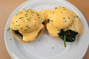 The yellow hollindaise sauce on top of two poached egg which are on a bed of spinach upon toasted english muffins. The dish is called Egg Florentine - 713572987