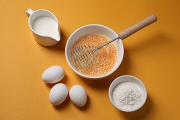 Fototapeta na wymiar Making dough. Beaten eggs in bowl, flour and milk on orange background, above view