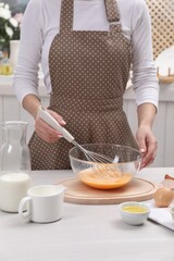 Woman whisking eggs in bowl at table indoors, closeup