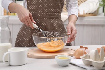 Woman whisking eggs in bowl at table indoors, closeup