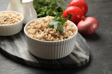 Tasty pearl barley porridge and parsley in bowl on dark textured table, closeup