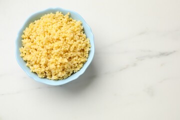 Tasty millet porridge in bowl on white marble table, top view. Space for text