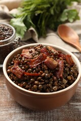 Delicious lentils with bacon in bowl on wooden table, closeup