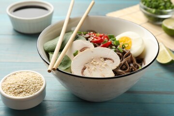 Tasty buckwheat noodles (soba) with chili pepper, egg, mushrooms and chopsticks on light blue wooden table, closeup