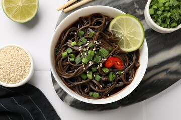 Tasty buckwheat noodles (soba) served on white table, flat lay