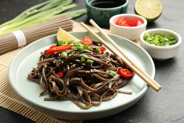 Tasty buckwheat noodles (soba) with chili pepper, onion and chopsticks on grey table, closeup