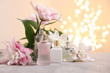 Bouquet of beautiful lily flowers and perfume bottles on table against beige background with blurred lights, closeup