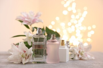 Perfume bottles and bouquet of beautiful lily flowers on table against beige background with blurred lights, closeup