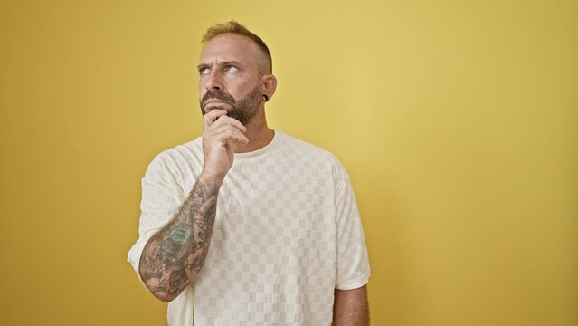 Handsome young man, looking lost in thought and smiling casually against an isolated yellow background, sparks an idea!