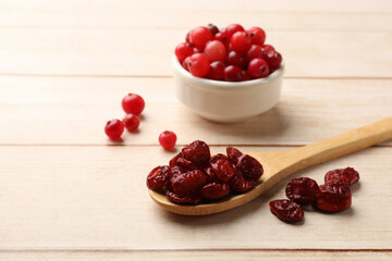 Spoon with dried cranberries and fresh berries in bowl on wooden table, space for text