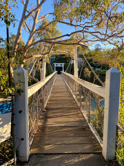Bridge over the river in forest. Structure of a pedestrian bridge on a sunny day. White gate and fenced walkway between two banks. 