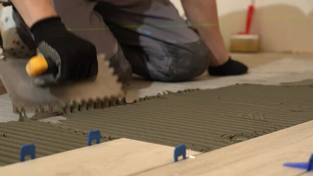 A tiler lays floor tiles on the floor. Porcelain tiles in the kitchen. A tiler is gluing tiles to the kitchen floor. A man is laying tiles on the bathroom floor.