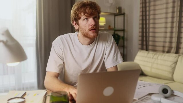 Busy red haired man student or freelancer with lack of new ideas or creative block typing deleting text and finding the idea on laptop computer at home workplace