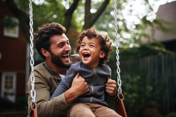 Father's Day. Diverse black dad with his son on a swing in backyard garden, smiling and looking...