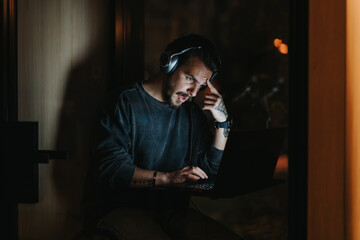 Focused man with headphones working late hours on laptop in office.
