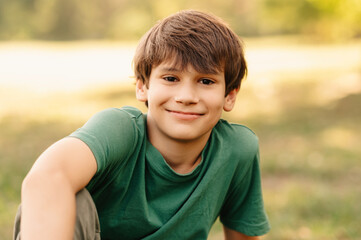 Close up portrait of a handsome teen boy smiling at the camera while sitting realxed on grass.