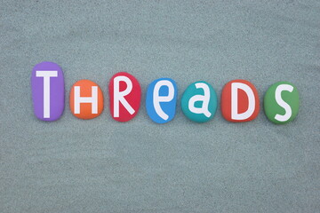 Threads, english word meaning discussions composed with hand painted multi colored stone letters over green sand