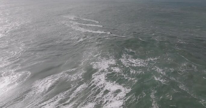 Aerial drone shot of jet ski riders in the Atlantic Ocean on a day with giant waves in Nazare, Portugal, Europe. Big wave surfing town. Drone rising and panning. Shot in ProRes 422 HQ