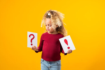 Fototapeta premium Enchanting Exploration. A Portrait of a Thoughtful child Girl Holding Cards with Question Marks and Exclamation Points.