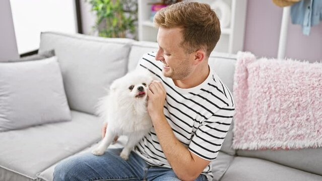 Cheerful young caucasian man confidently relaxing with his happy dog on a cozy sofa, enjoying his comfortable home interior with a joyful smile.