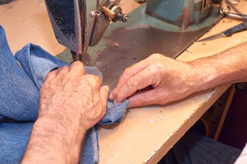 Hands of a tailor sewing blue jeans on a sewing machine