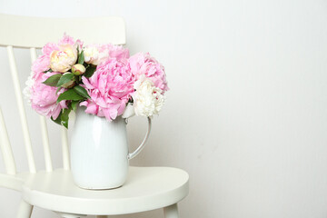Beautiful peonies in jug on white chair. Space for text