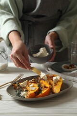 Woman putting cheese on baked pumpkin slices at table, closeup
