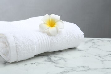 Fototapeta na wymiar Folded terry towel and plumeria flower on white marble table, closeup. Space for text