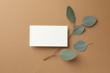 Blank business card and eucalyptus branch on beige background, top view. Mockup for design