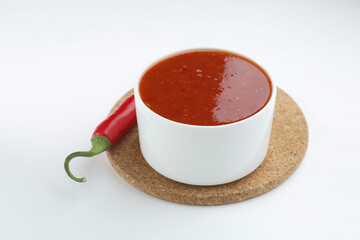 Spicy chili sauce in bowl and fresh pepper on white background