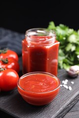 Delicious ketchup on black wooden table, closeup. Tomato sauce