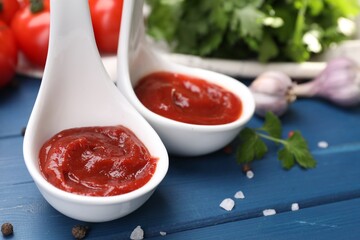Organic ketchup in spoons and spices on blue wooden table, closeup. Tomato sauce