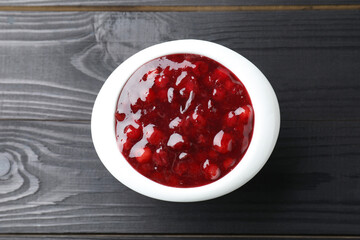 Fresh cranberry sauce in bowl on black wooden table, top view