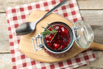 Fresh cranberry sauce in glass jar, rosemary and spoon on light wooden table, top view