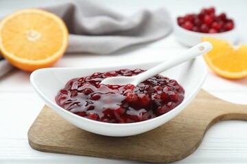 Fresh cranberry sauce in bowl and spoon on white wooden table, closeup