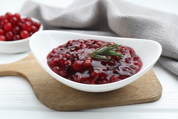 Fresh cranberry sauce and rosemary in bowl on white wooden table, closeup