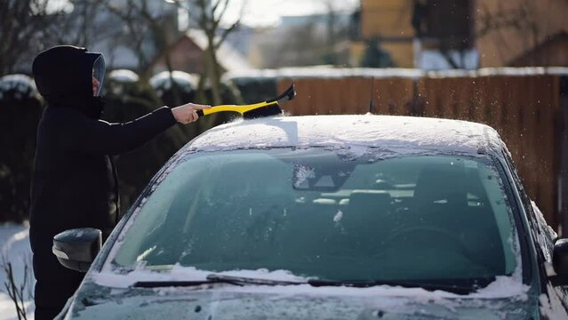 Woman Cleaning Car from Snow in Winter. Person Brushing Snow off the Car Roof with a Brusher Scraper	