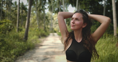 Woman close up portrait enjoy tropical forest walk in sunny day. Hiking trail and green coconuts. Beautiful path among large palm trees. Outdoor lifestyle travel, summer holiday vacation
