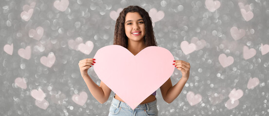 Beautiful young woman with pink paper heart on grey background with glowing lights. Valentines Day celebration