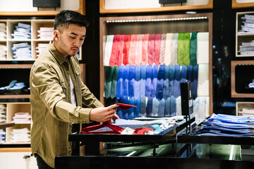 Man Evaluating Necktie Options in a Store - obrazy, fototapety, plakaty
