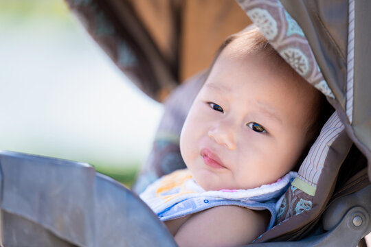 Baby Relaxing in a Stroller Outside. Toddler Boy with slight smile rests, looking out with curious eyes, enjoying the comfort and sights of a leisurely day outdoors. Asian Child aged 1 years old.