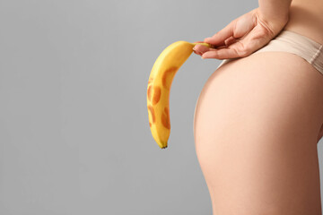 Woman holding banana with lipstick kiss marks on light background, closeup. Sex concept