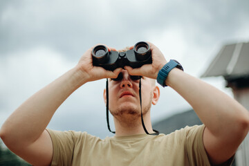 The young man is scrutinizing something through binoculars.